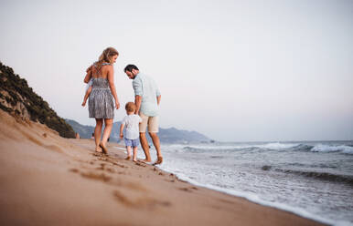 Rückansicht einer jungen Familie mit zwei Kleinkindern, die im Sommerurlaub am Strand spazieren gehen. - HPIF23844