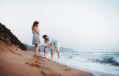 Eine junge Familie mit zwei Kleinkindern steht im Sommerurlaub am Strand und hat Spaß. - HPIF23845