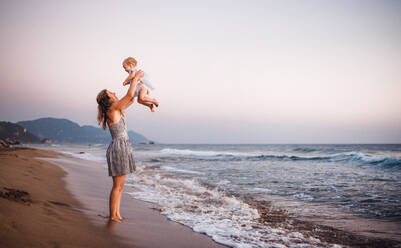 Eine junge Mutter mit einem Kleinkind am Strand im Sommerurlaub, die Spaß haben. - HPIF23846