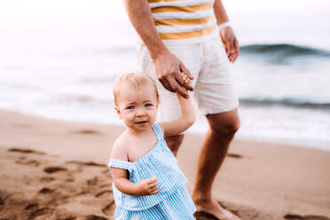 Mittelteil eines Vaters mit einem kleinen Mädchen, das im Sommerurlaub am Strand spazieren geht. - HPIF23860
