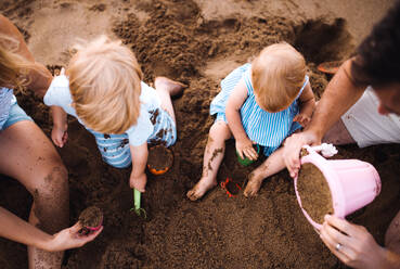 Eine junge Familie mit Kleinkindern, die im Sommerurlaub am Strand mit Sand spielen, von oben und von der Mitte aus gesehen. - HPIF23861