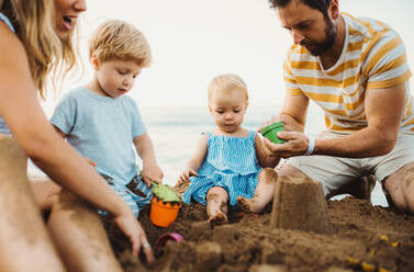 Eine junge Familie mit Kleinkindern spielt im Sommerurlaub am Strand mit Sand. - HPIF23862