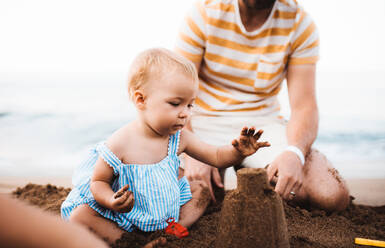 Mittelteil eines Vaters mit einem Kleinkind, das am Strand im Sommerurlaub spielt. - HPIF23863