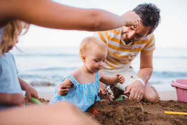 Eine junge Familie mit Kleinkindern spielt im Sommerurlaub am Sandstrand. - HPIF23864