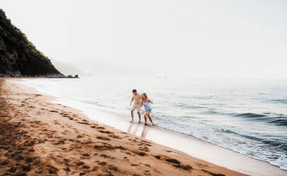 Ein fröhlicher Mann und eine fröhliche Frau, die im Sommerurlaub am Strand spazieren gehen und sich an den Händen halten. Copy space. - HPIF23873
