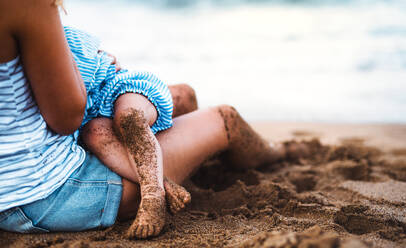 Ein Mittelteil einer nicht erkennbaren jungen Mutter, die ihre kleine Tochter am Strand im Sommerurlaub stillt. - HPIF23879