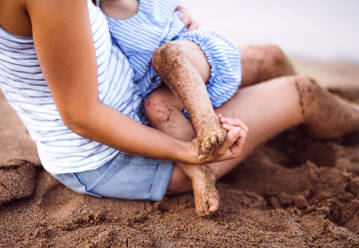 A midsection of breasfeeding toddler daughter on beach on summer holiday. - HPIF23880