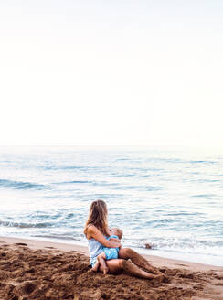 Eine junge Mutter stillt ihre kleine Tochter am Strand im Sommerurlaub. - HPIF23882