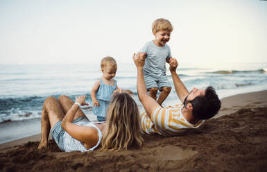 A family with two toddler children lying on sand beach on summer holiday, playing. - HPIF23885