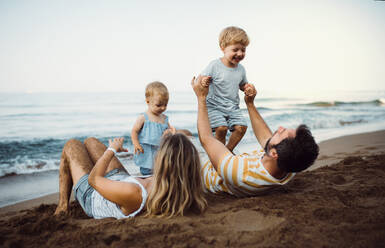 Eine Familie mit zwei Kleinkindern liegt im Sommerurlaub am Sandstrand und spielt. - HPIF23885