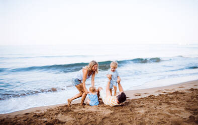 A family with two toddler children lying on sand beach on summer holiday, playing. - HPIF23886
