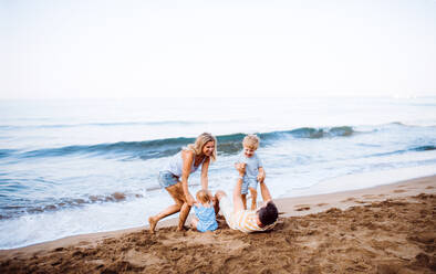 Eine Familie mit zwei Kleinkindern liegt im Sommerurlaub am Sandstrand und spielt. - HPIF23886