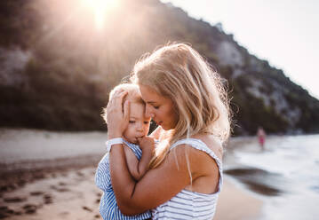 Junge Mutter, die ein kleines Mädchen am Strand im Sommerurlaub bei Sonnenuntergang umarmt. - HPIF23894