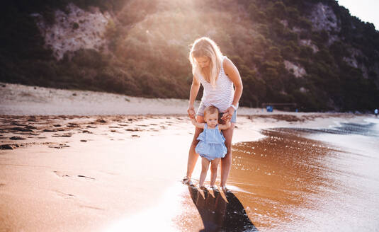 Young mother walking with a toddler girl on beach on summer holiday at sunset. - HPIF23896