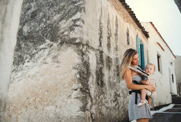 A young mother with a baby in a carrier walking in town on summer holiday. Copy space. - HPIF23905