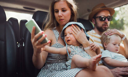 Eine junge Familie mit zwei Kleinkindern im Taxi im Sommerurlaub, die ihr Smartphone benutzen. - HPIF23913