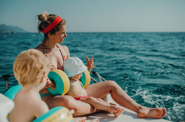 Eine Mutter und zwei Kleinkinder mit Armbändern sitzen im Sommerurlaub am Strand. - HPIF23918