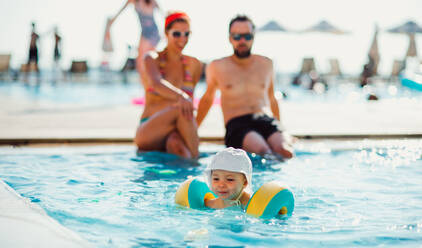 Ein kleines Kleinkind mit Armbändern und Eltern im Schwimmbad im Sommerurlaub. - HPIF23922