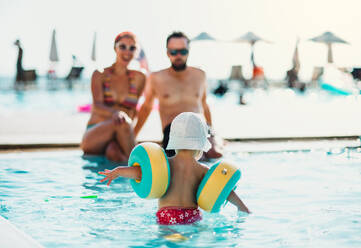 Ein kleines Kleinkind mit Armbändern und Eltern im Schwimmbad im Sommerurlaub. - HPIF23923