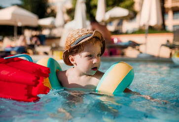 Ein glücklicher kleiner Junge mit Armbändern, der im Sommerurlaub im Wasser schwimmt. - HPIF23924