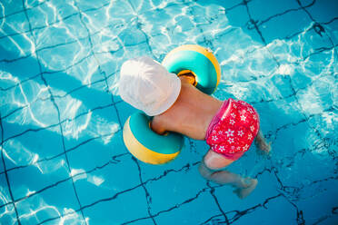 Blick von oben auf ein kleines Kind mit Armbändern im Schwimmbad im Sommerurlaub. - HPIF23926