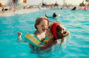 Ein glücklicher kleiner Junge mit Armbändern und seine Mutter beim Schwimmen im Wasser im Sommerurlaub. - HPIF23928