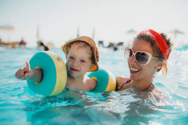 Ein glücklicher kleiner Junge mit Armbändern und seine Mutter beim Schwimmen im Wasser im Sommerurlaub. - HPIF23929