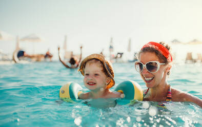 Ein glücklicher kleiner Junge mit Armbändern und seine Mutter beim Schwimmen im Wasser im Sommerurlaub. - HPIF23930