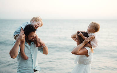 Eine junge Familie mit zwei Kleinkindern steht lachend am Strand im Sommerurlaub. - HPIF23961