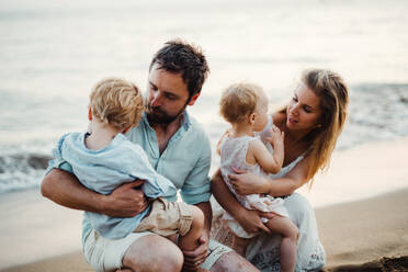 Eine Familie mit zwei Kleinkindern sitzt im Sommerurlaub am Sandstrand und spielt. - HPIF23966