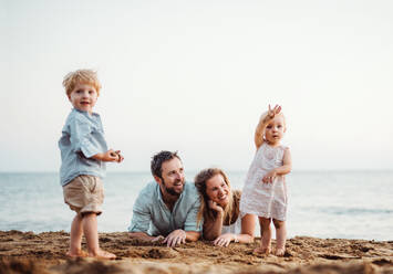 Eine Familie mit zwei Kleinkindern liegt im Sommerurlaub am Sandstrand und spielt. - HPIF23970