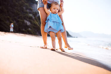 Midsection der jungen Mutter zu Fuß mit einem Kleinkind Mädchen am Strand im Sommerurlaub bei Sonnenuntergang. - HPIF23974
