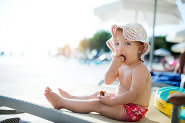 A cute small toddler girl sitting on beach on summer holiday. Copy space. - HPIF23977