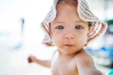 A close-up of cute small toddler girl sitting on beach on summer holiday. - HPIF23978