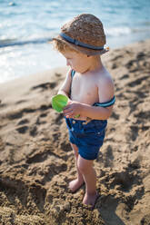 Ein beschäftigtes kleines Kleinkind, das im Sommerurlaub am Strand sitzt und spielt. - HPIF23980