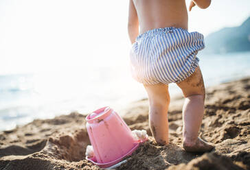 Ein Mittelteil eines kleinen Mädchens mit Shorts, das im Sommerurlaub am Sandstrand spielt, in der Rückansicht. - HPIF23982