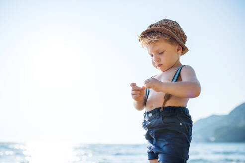 Ein kleiner Junge mit Hut und Shorts steht im Sommerurlaub am Strand und kopiert den Raum. - HPIF23984