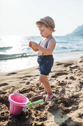 Ein beschäftigtes kleines Kleinkind, das im Sommerurlaub am Strand sitzt und spielt. - HPIF23985