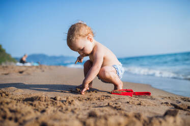 Ein kleines topless Kleinkind Mädchen sitzt am Strand im Sommerurlaub, spielen im Sand. - HPIF23987