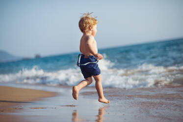 A cute small toddler boy with shorts running on sand beach on summer holiday. Copy space. - HPIF23989