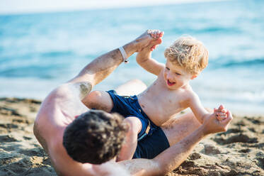 A father with a happy toddler son playing on sand beach on summer holiday. - HPIF23991