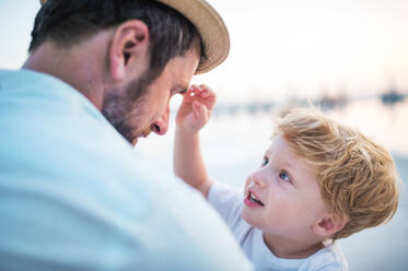 Ein reifer Vater hält ein Kleinkind am Strand im Sommerurlaub. - HPIF24002