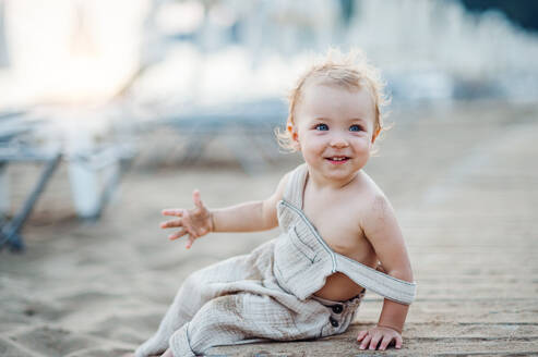 Eine niedliche kleine Kleinkind Mädchen sitzt am Strand im Sommerurlaub. kopieren Raum. - HPIF24006