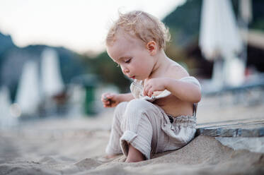 Eine niedliche kleine Kleinkind Mädchen sitzt am Strand im Sommerurlaub. kopieren Raum. - HPIF24010
