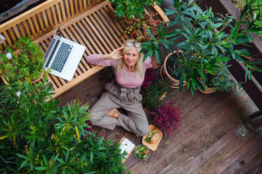 Top view of senior woman with laptop conmputer sitting outdoors on terrace, resting. - HPIF24026