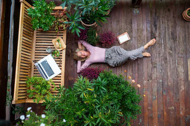 A top view of senior woman with laptop lying outdoors on terrace, resting. - HPIF24028