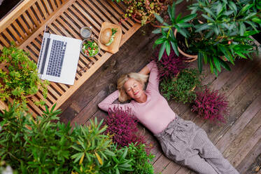 Draufsicht auf eine ältere Frau mit Laptop, die im Freien auf einer Terrasse liegt und sich ausruht. - HPIF24030