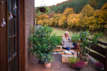 Senior woman with laptop and smartphone sitting outdoors on terrace, working. - HPIF24045