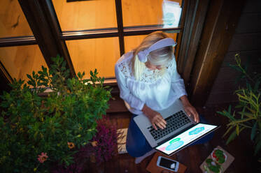 Eine ältere Frau mit Laptop sitzt auf der Terrasse und arbeitet am Abend. - HPIF24058