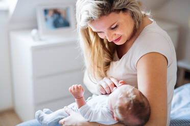 Eine schöne junge Mutter, die ihr neugeborenes Baby zu Hause im Arm hält. - HPIF24061